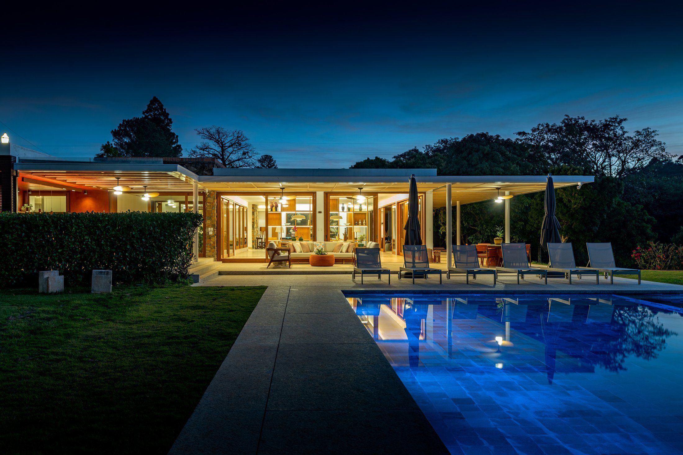 Residência de alto padrão iluminada ao anoitecer, com piscina refletindo o estar aberto