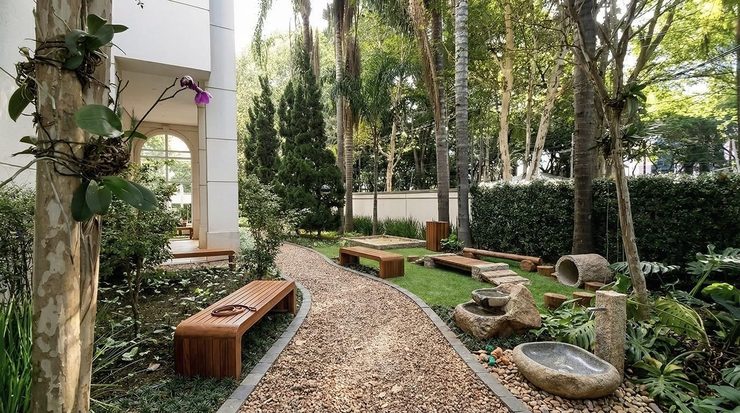 Área comum de condomínio requalificada com jardim, bancos de madeira e caminho de seixos